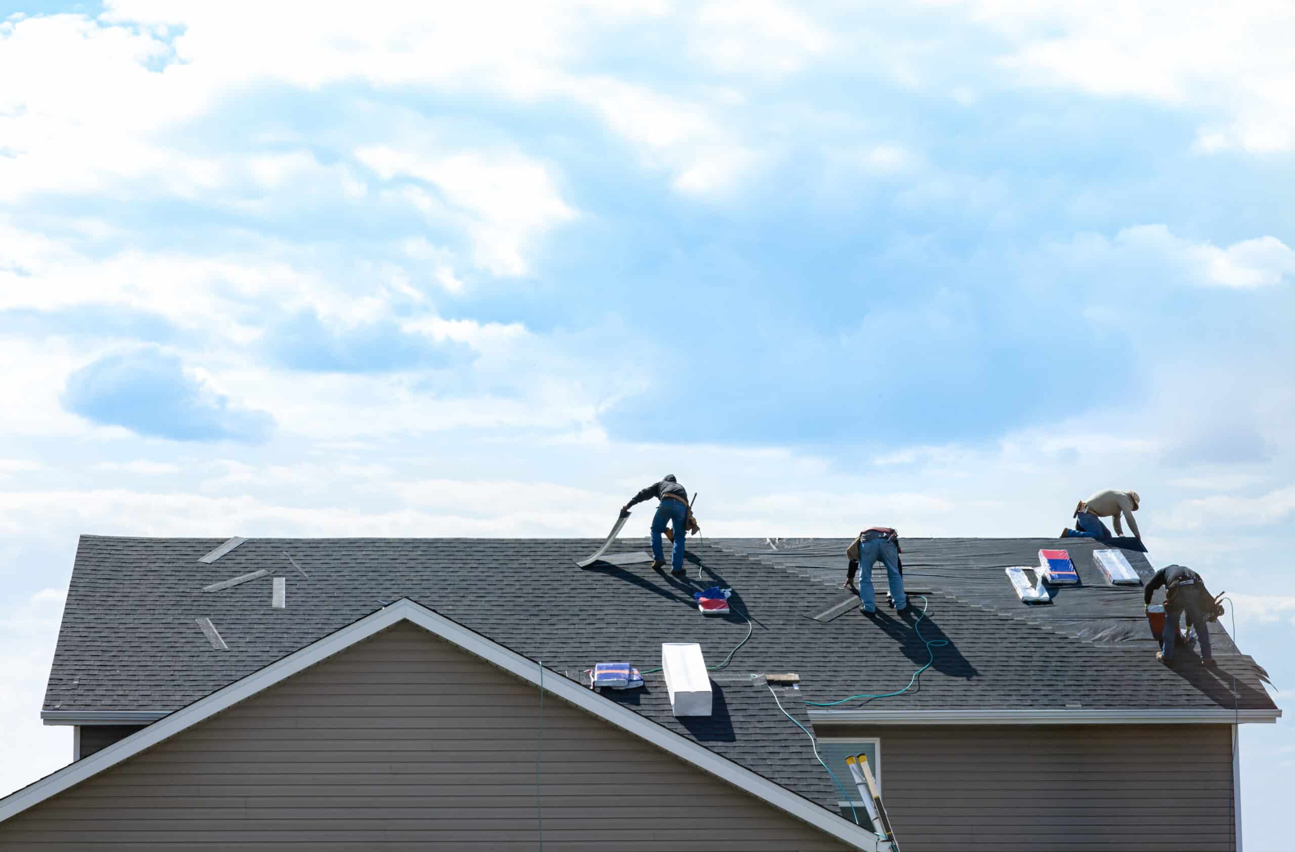 4 construction workers fixing roof against clouds blue sky.