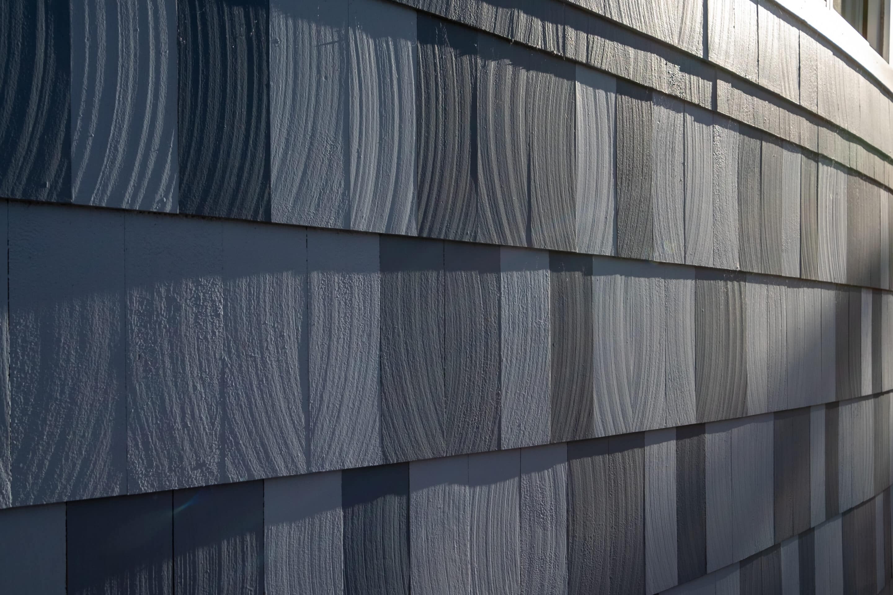 The exterior of a grey colored faux cedar composite wall. The gray plastic material is eco-friendly polymer tiles in rows and layers. The design is contemporary with a natural wood grain surface. The exterior of a grey colored faux cedar composite wall. The gray plastic material is eco-friendly polymer tiles in rows and layers. The design is contemporary with a natural wood grain surface.