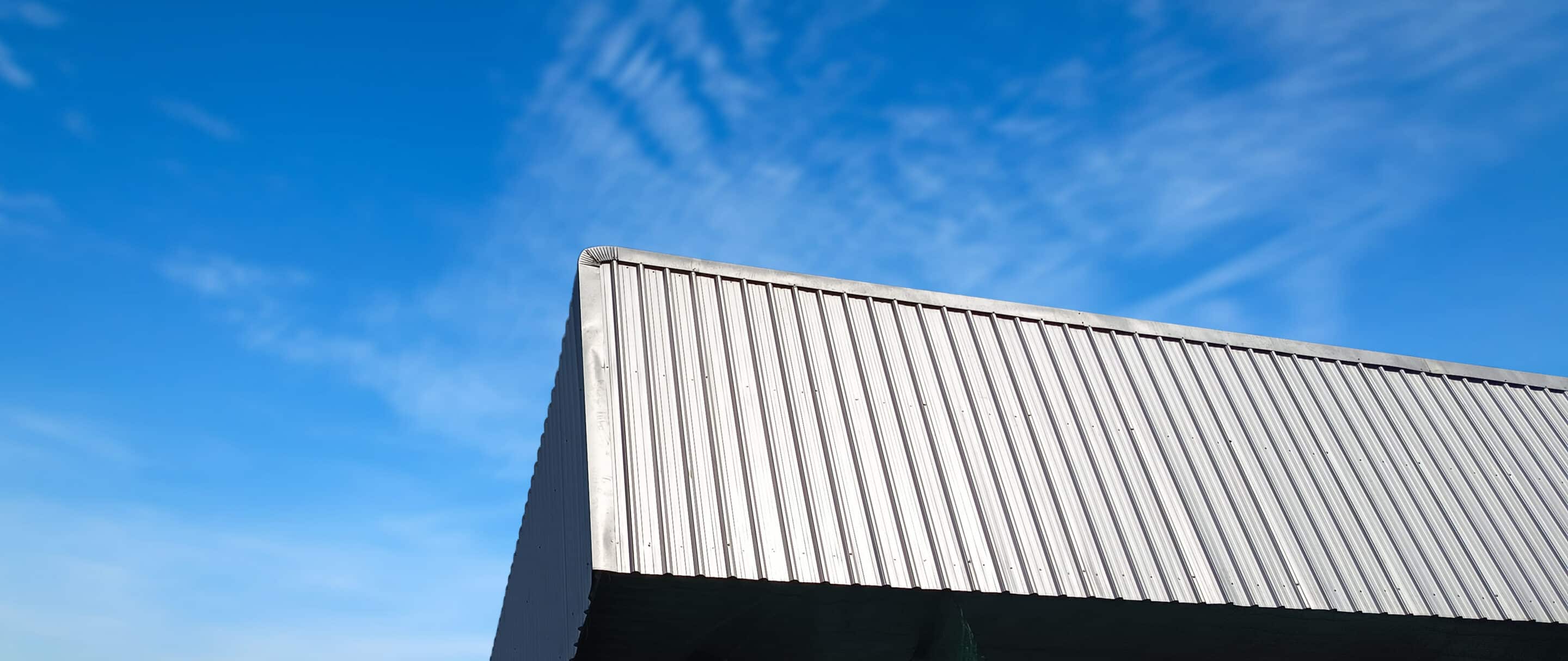 Metal sheet roof curve on blue sky. Modern construction, Metal ribbed arch span roof covering, Large building roof Metal sheet roof curve on blue sky. Modern construction, Metal ribbed arch span roof covering large roof